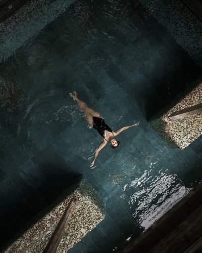 Frau schwimmt entspannt auf dem Rücken in einem Innenpool mit Mosaikfliesen