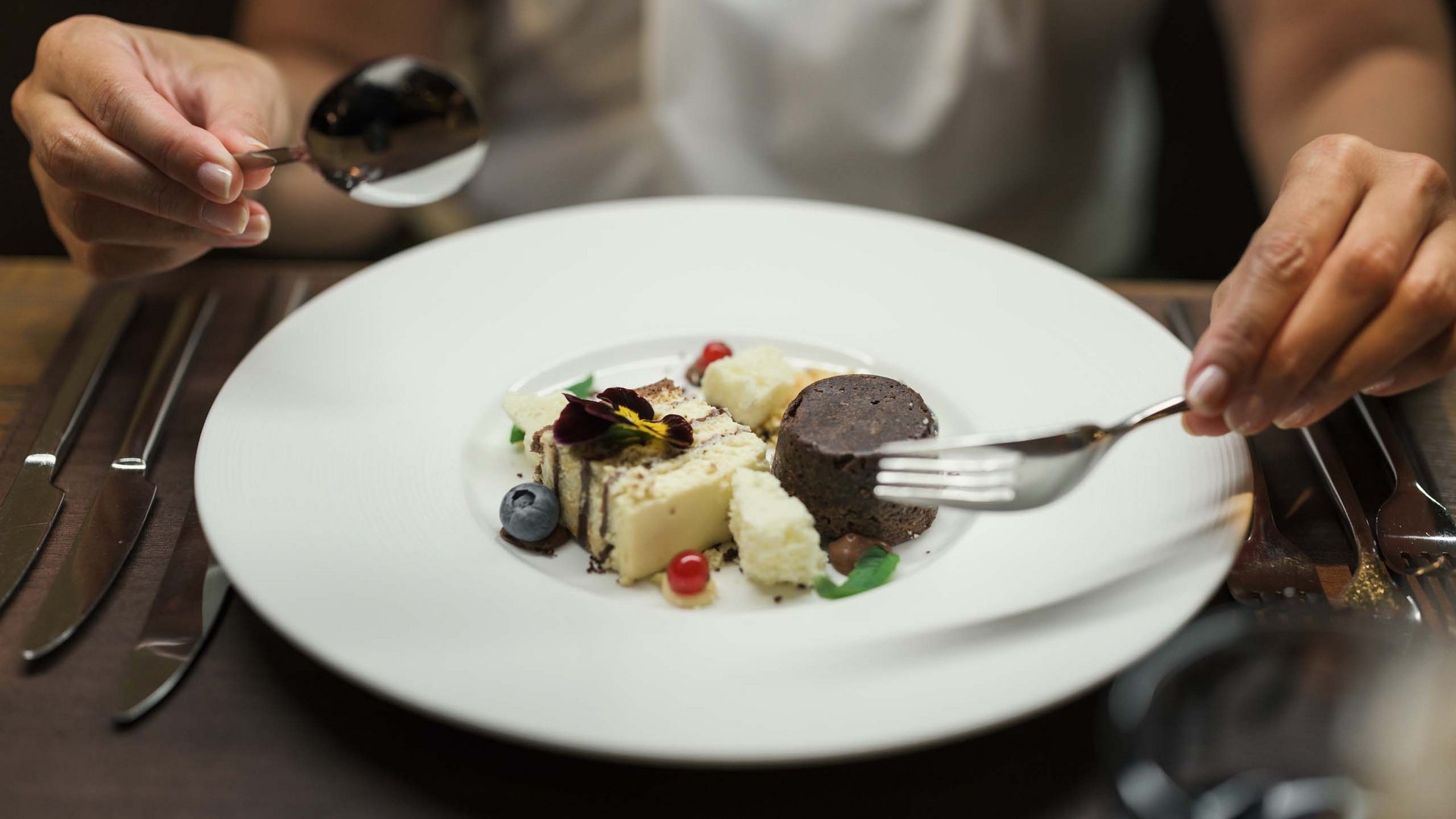 Wellness und Luxus: Ihr Hotel in Tirol Person isst fein angerichtetes Dessert mit Gabel und Löffel