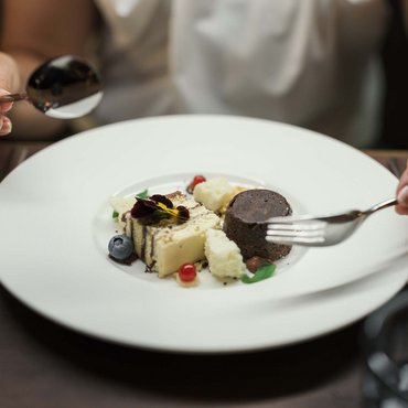 Person isst fein angerichtetes Dessert mit Gabel und Löffel