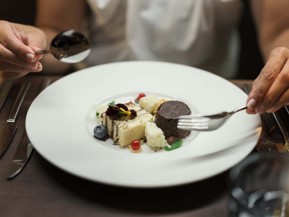 Person isst fein angerichtetes Dessert mit Gabel und Löffel