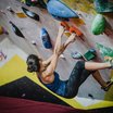 Frau klettert an einer Indoor-Boulderwand mit bunten Griffen