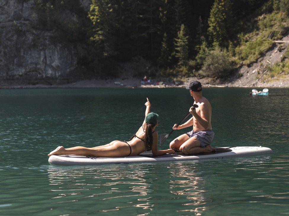 Paar auf einem Paddleboard auf ruhigem Bergsee umgeben von Tannen