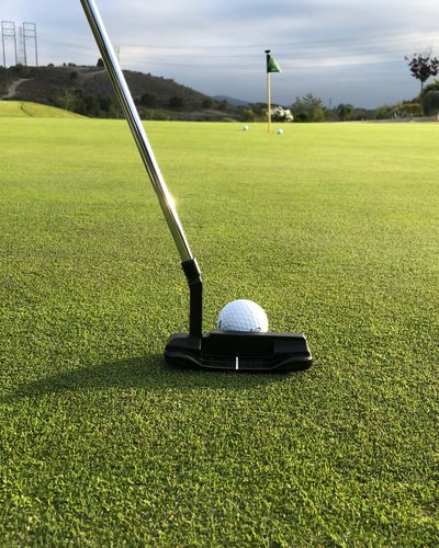 Golfball auf Grün mit Putter und Fahne im Hintergrund