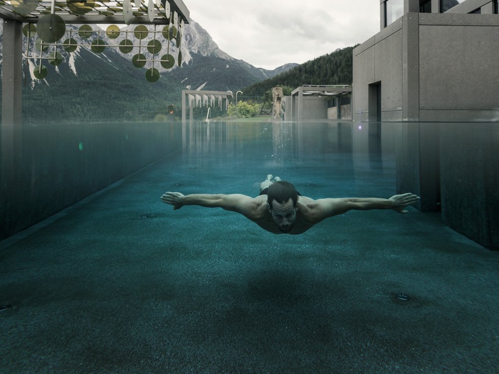 Mann schwimmt unter Wasser in modernem Pool mit Bergblick