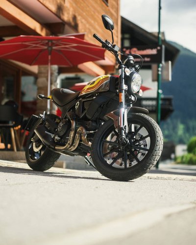 Schwarzes und gelbes Motorrad auf Gehweg vor Café mit rotem Sonnenschirm