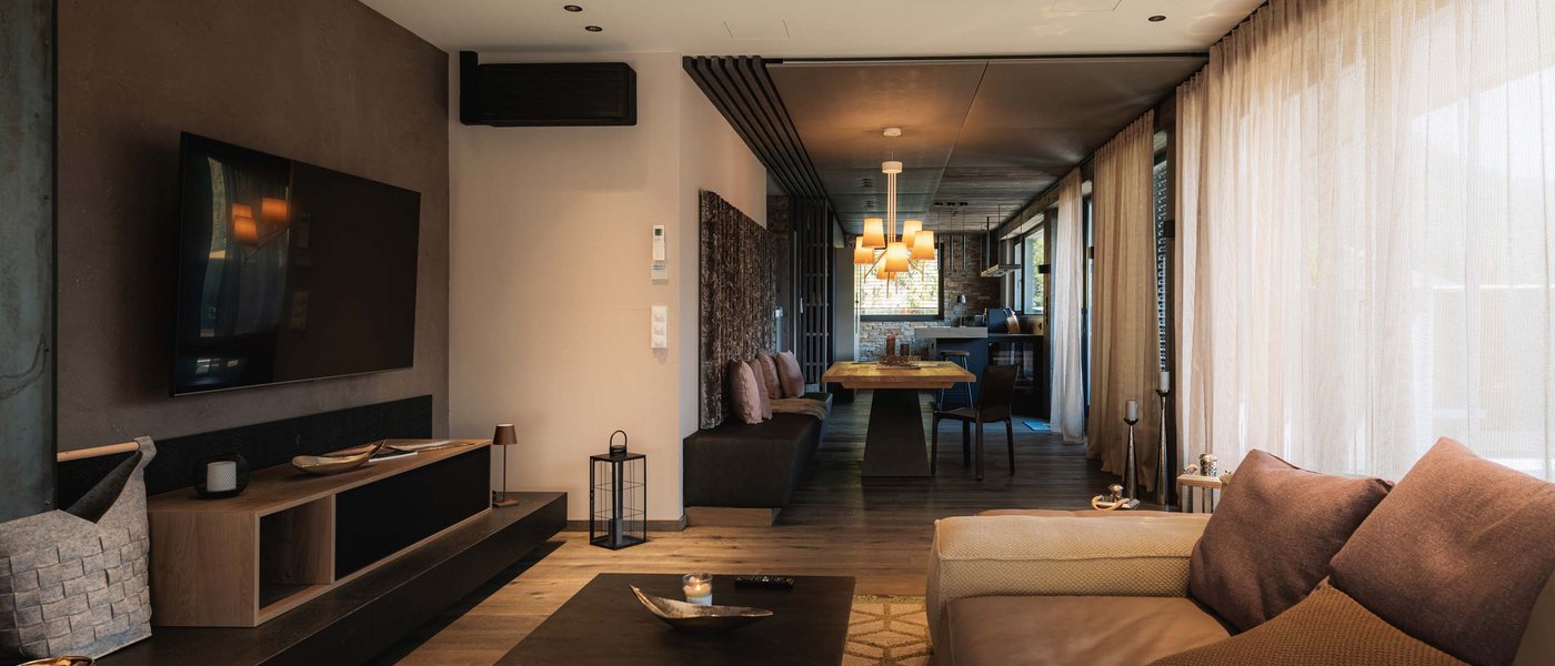 Modernes Wohnzimmer mit brauner Couch, TV und Essbereich im Hintergrund