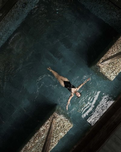 Frau im schwarzen Badeanzug liegt entspannt auf dem Wasser in einem Pool