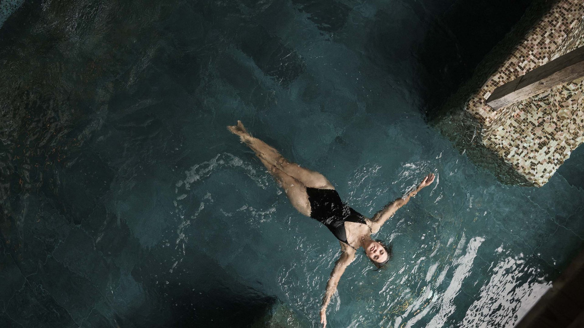 Frau im schwarzen Badeanzug liegt entspannt auf dem Wasser in einem Pool
