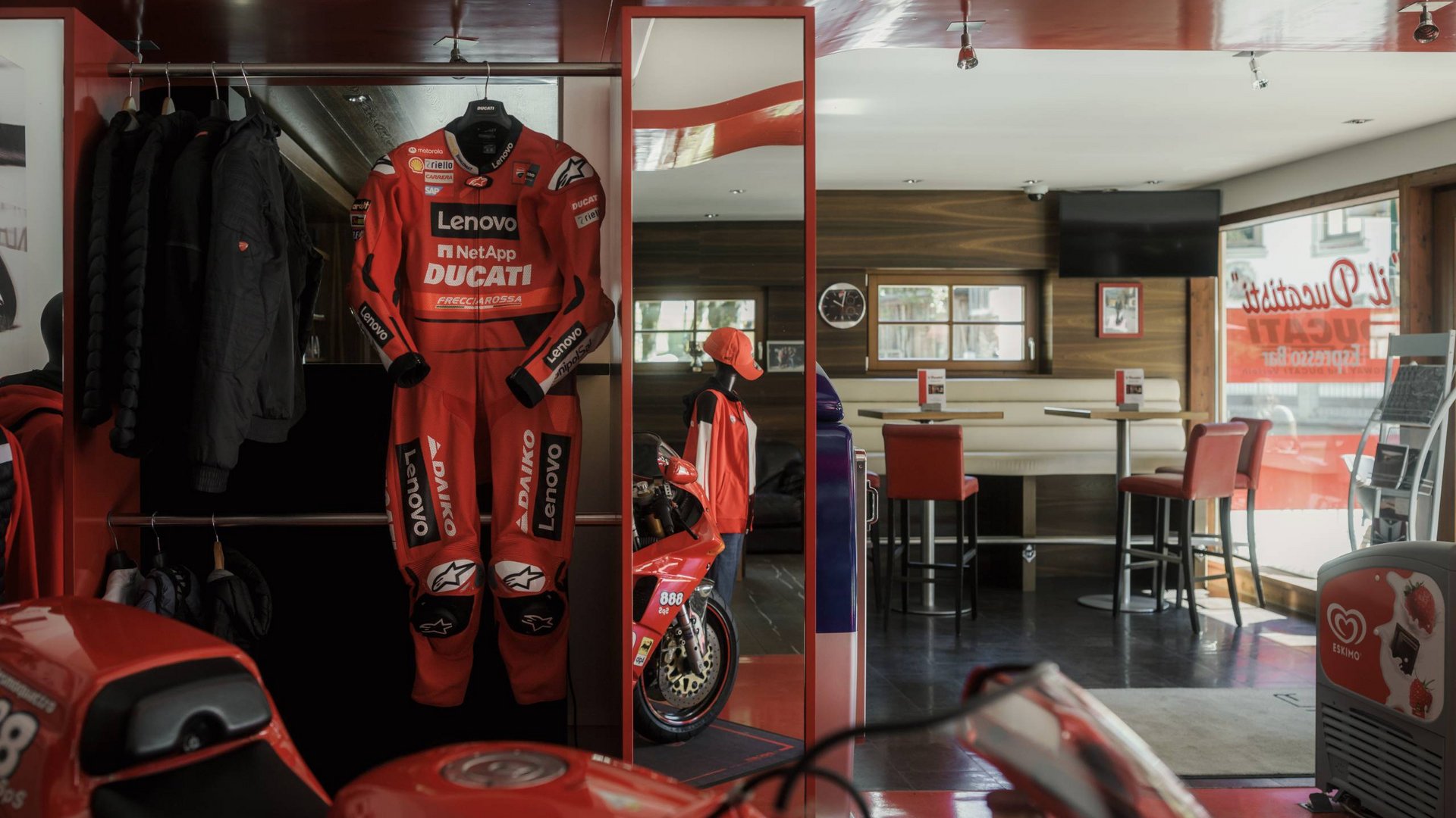Rotes Ducati-Rennanzug und Motorrad in einem Café mit Sitzbereich