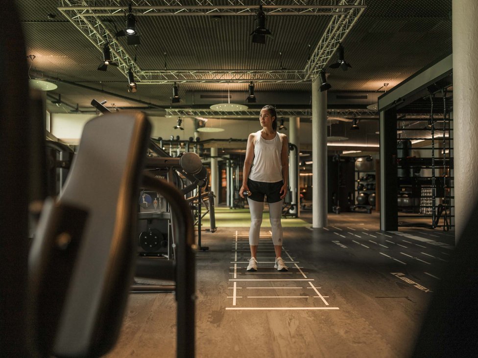 Frau im Fitnessstudio hält Hantel und steht auf markiertem Boden