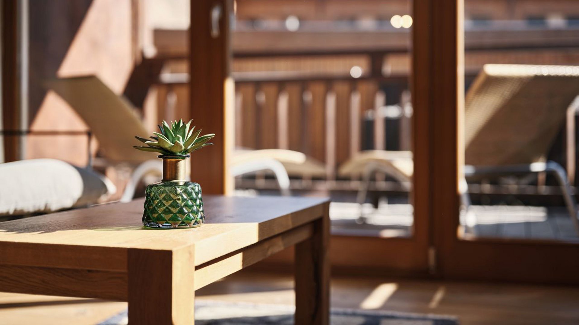 Grüne Pflanze in Glasvase auf Holztisch vor Balkon mit Liegestühlen