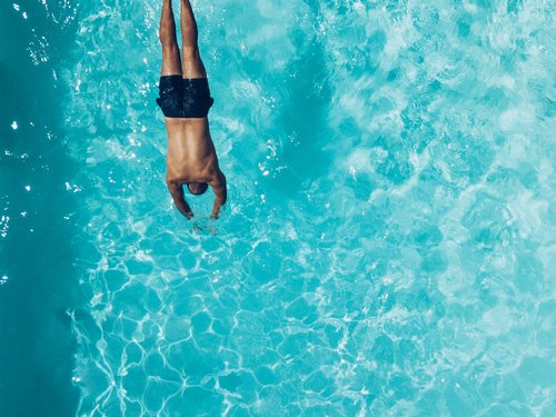 Mann taucht kopfüber in einen klaren blauen Pool