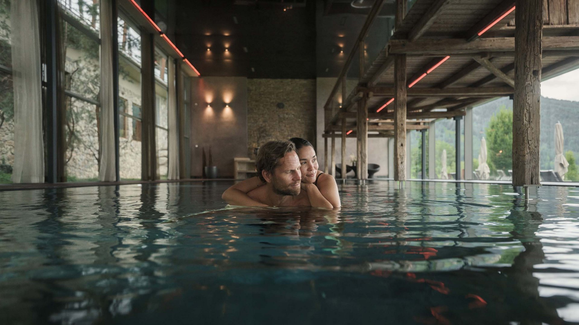 Paar entspannt sich in einem innenliegenden Hotelpool mit Holzbalken und großen Fenstern