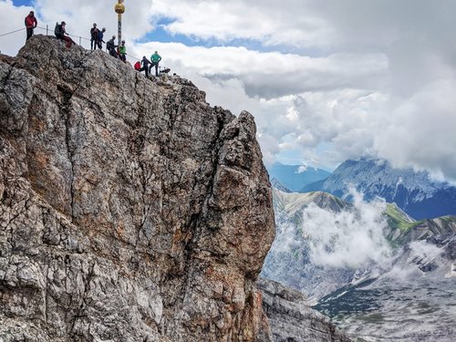 Berggipfel mit Wanderern und Gipfelkreuz unter bewölktem Himmel