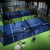 Indoor-Padel-Tennisplätze mit Spielern und Sitzbereich auf grünem Teppich