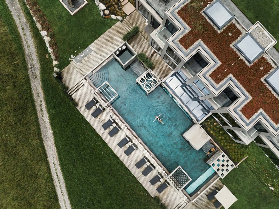 Luftaufnahme eines Pools mit Person und Liegestühlen neben modernem Gebäude
