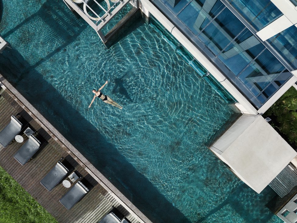 Frau schwimmt entspannt in einem modernen Außenpool neben einem Gebäude