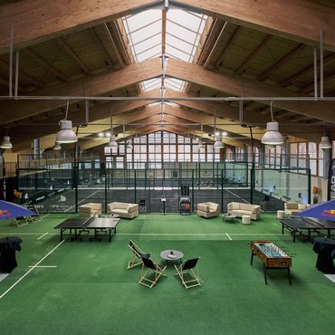 Indoor padel courts with players and seating area on green flooring