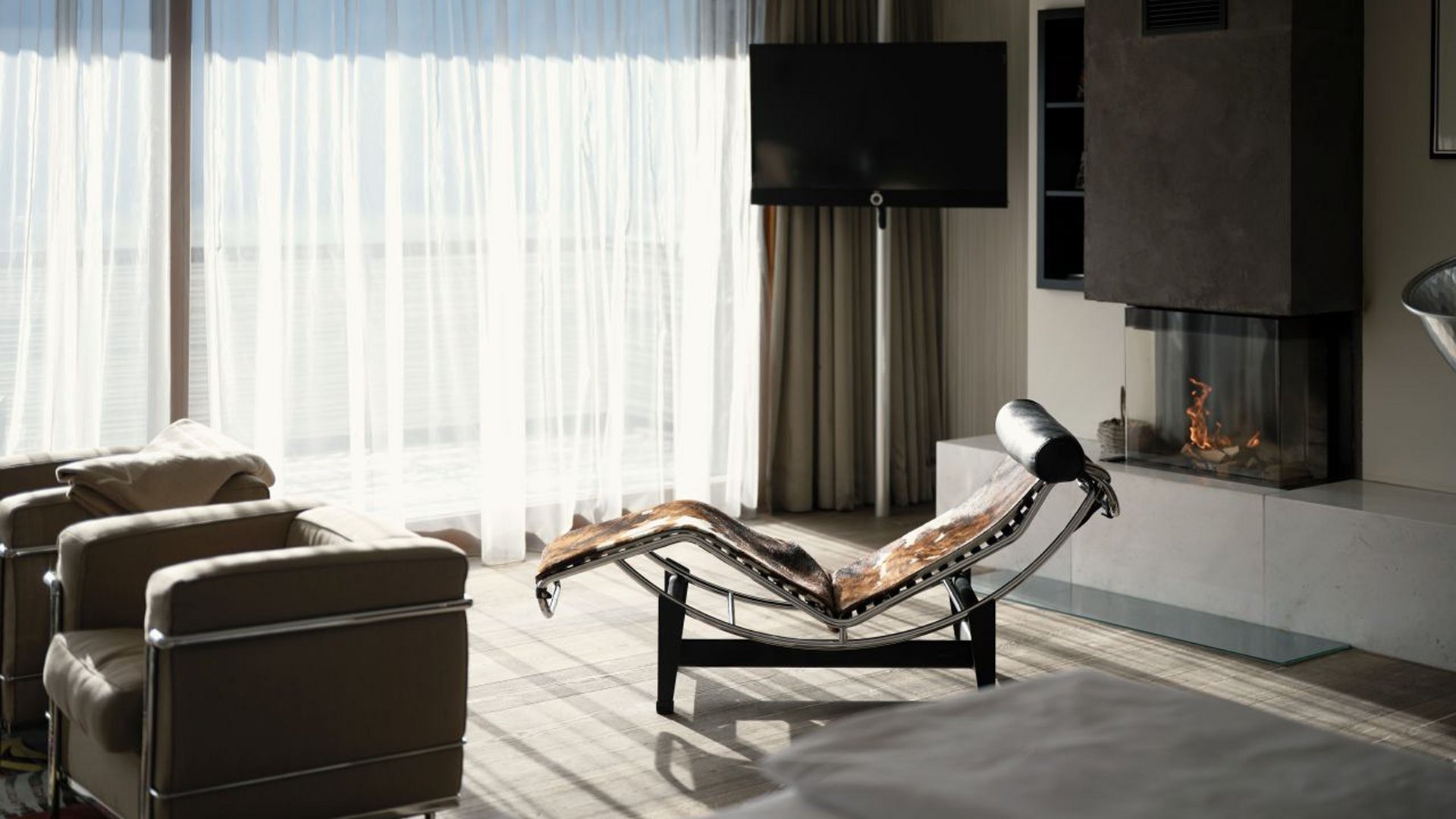 Moderner Wohnbereich mit Ledersesseln, Liege und Kamin vor großen Fenstern