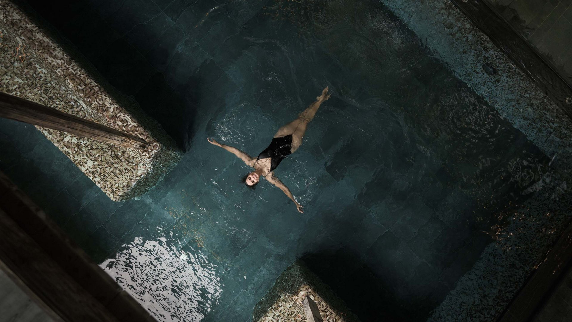 Frau entspannt und treibt auf dem Rücken in einem dunklen Schwimmbad