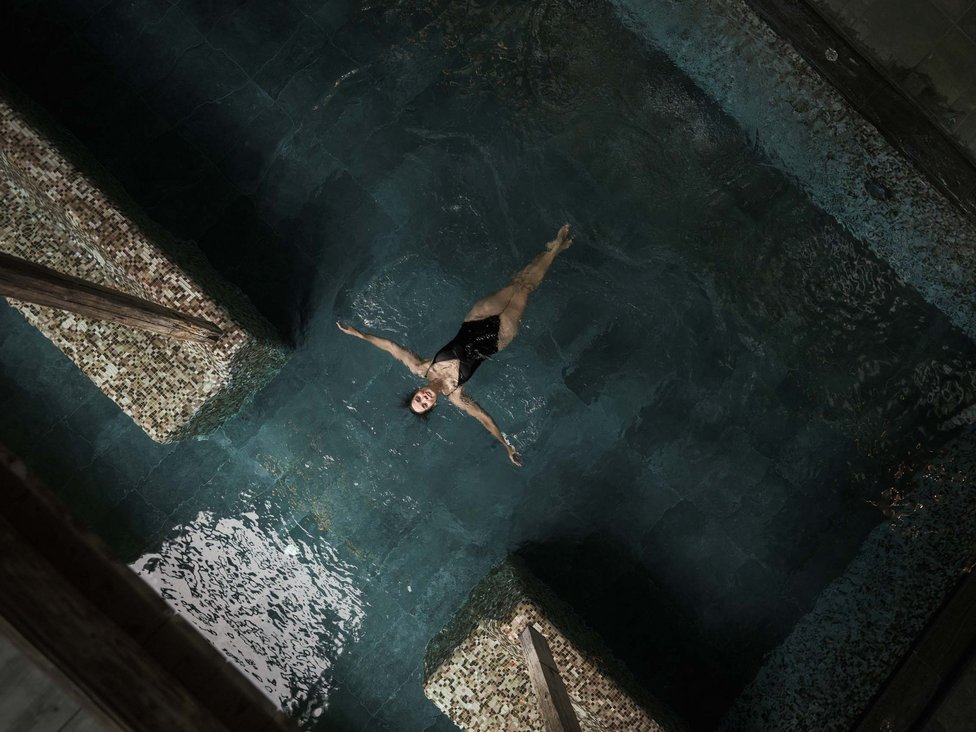 Wellness und Luxus: Ihr Hotel in Tirol Frau entspannt und treibt auf dem Rücken in einem dunklen Schwimmbad