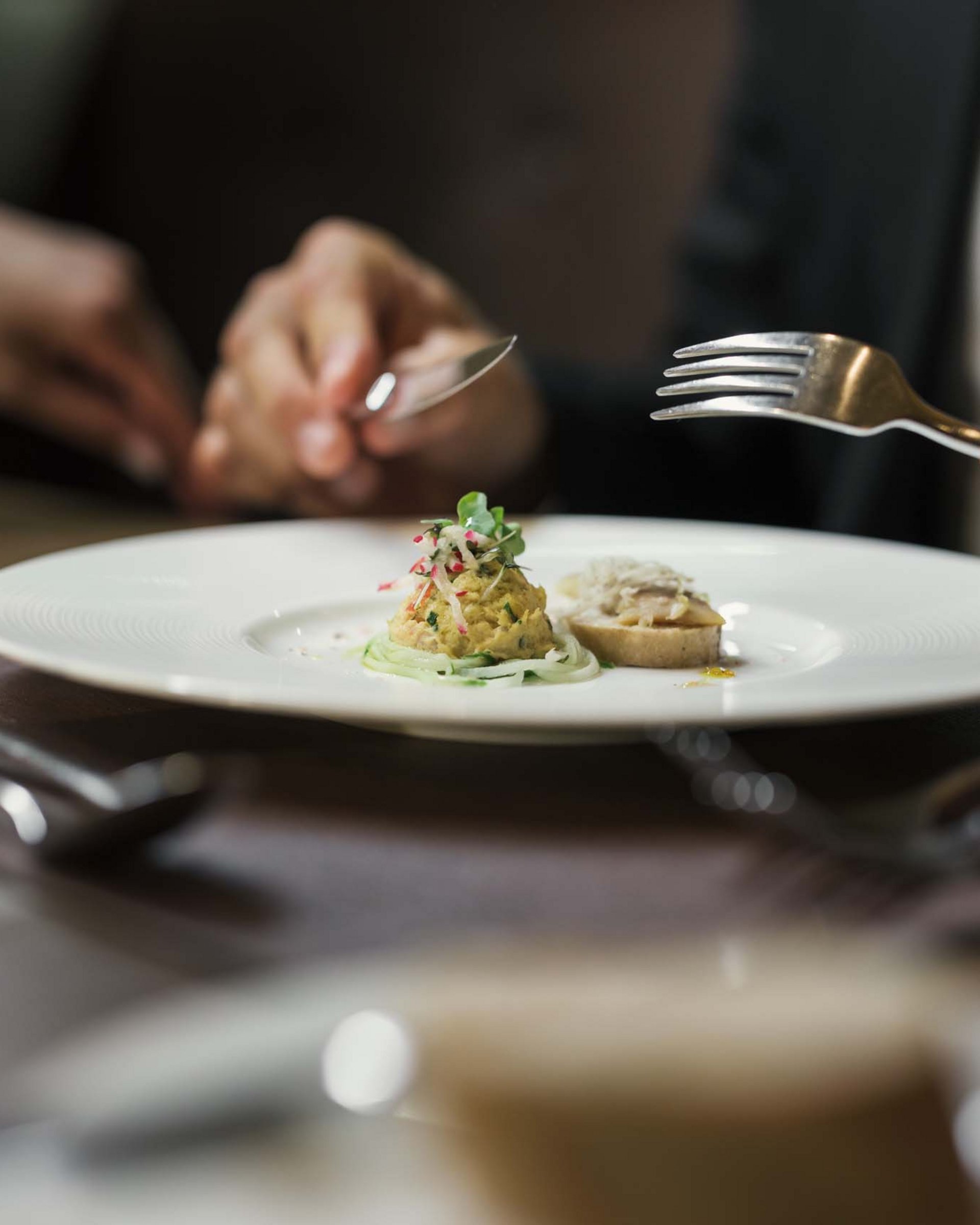 Wandern in und rund um Lermoos Person hält Besteck vor kleinem Gourmetgericht auf weißem Teller
