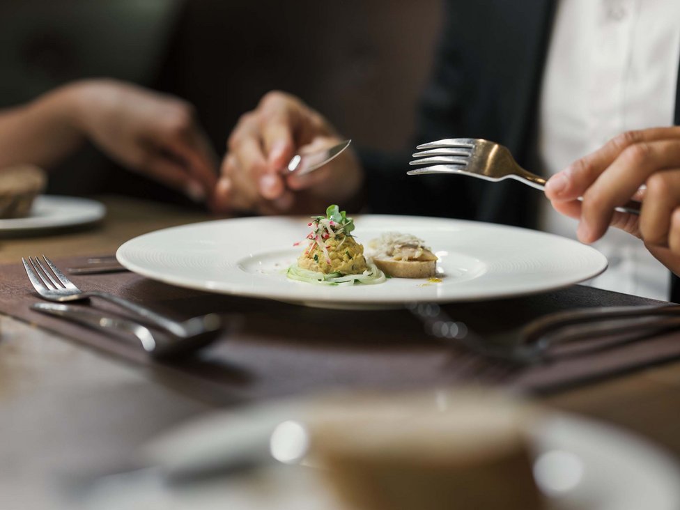 Wellness und Luxus: Ihr Hotel in Tirol Person hält Besteck vor kleinem Gourmetgericht auf weißem Teller