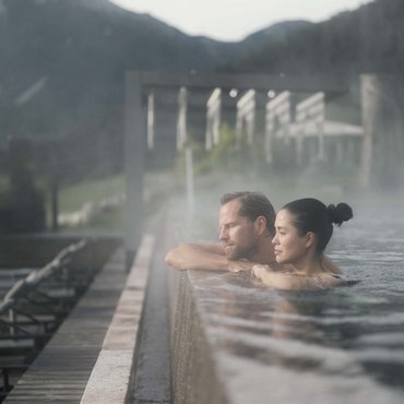 Couple relaxing in heated outdoor pool with mountain view.